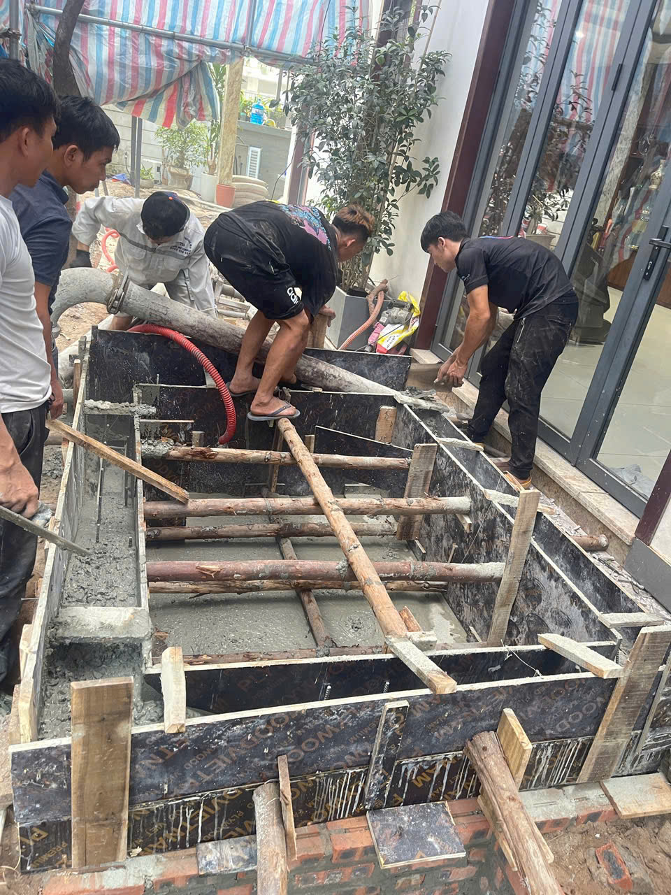 Công nhân đang đổ bê tông cho bể xây dựng ngoài trời trước cửa nhà